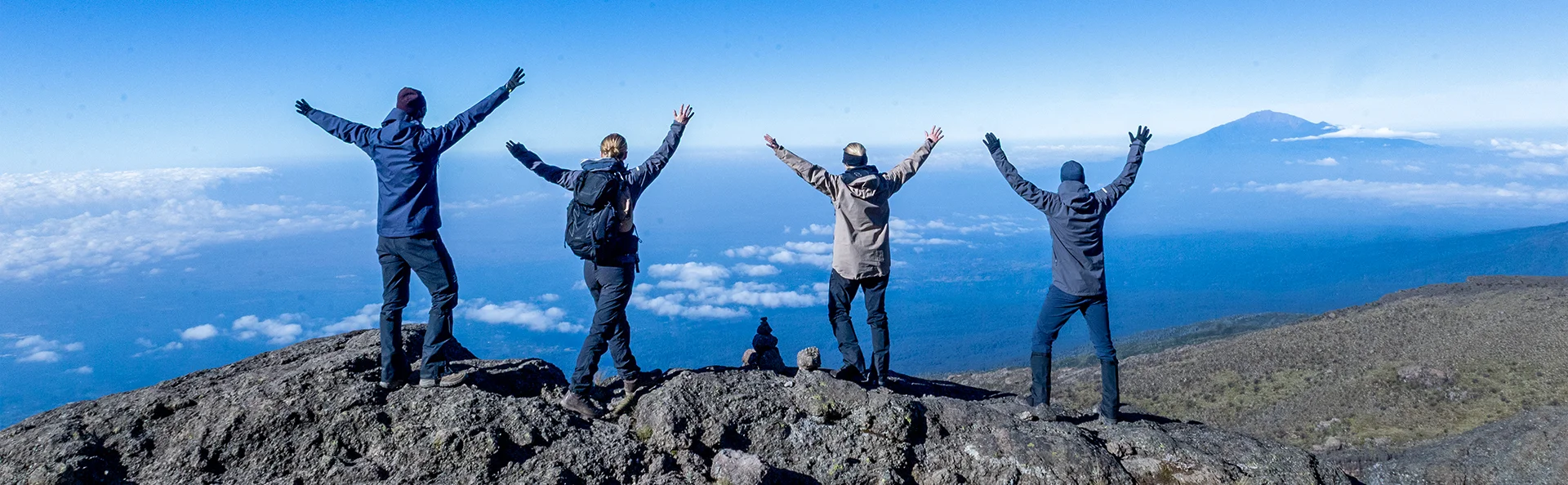 En grupp står med lyfta armar på toppen av Kilimanjaro