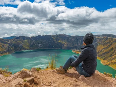 En kvinna sitter vid kanten av kratersjön Quilotoa i Ecuador.