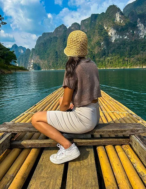 En kvinna färdas på en bambuflotte på en sjö i Thailand, omgiven av dramatiska kalkstensberg.